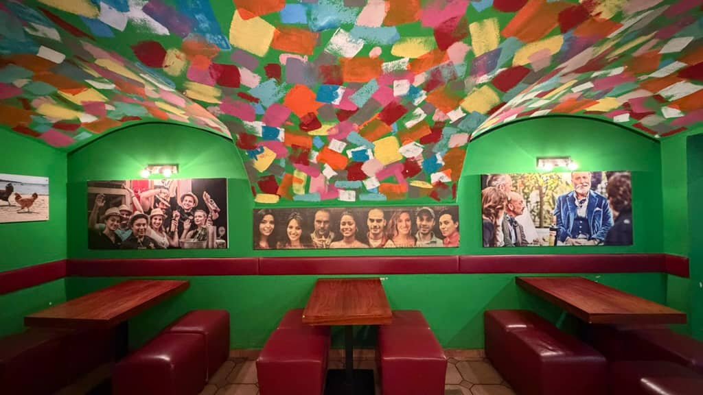 Bar-Innenraum mit grünen Wänden, bunten Farbtupfern und der Decke und Porträtfotos.