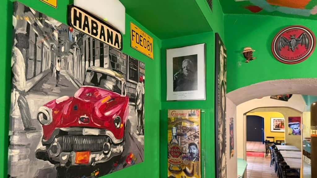 Grüner Balken mit kubanischen Dekoelementen, einem roten Oldtimer-Gemälde und Porträtfotos.